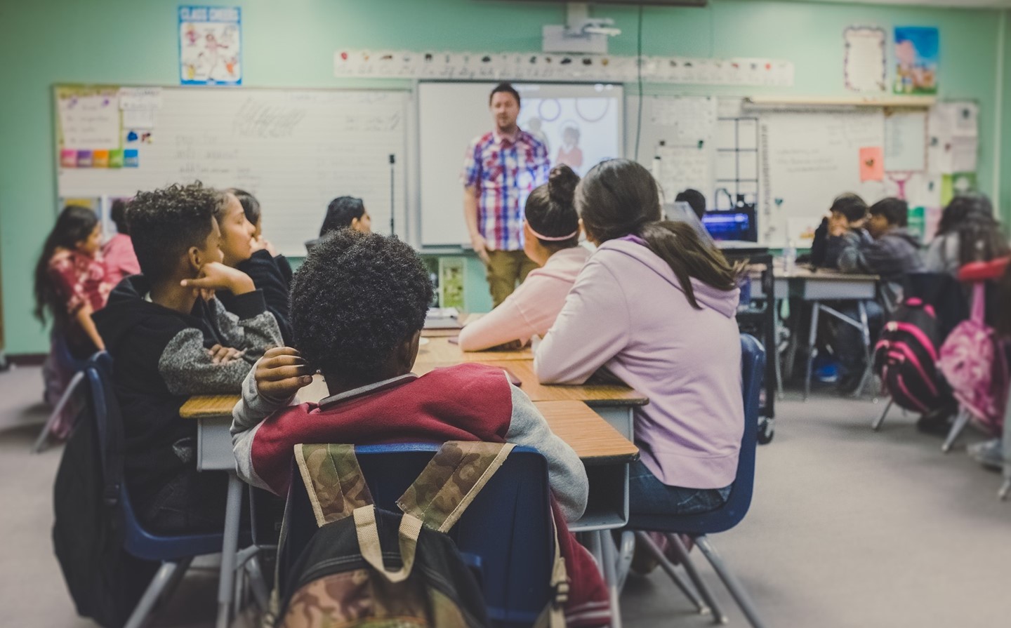 Students sitting at desks, listening to a teacher.