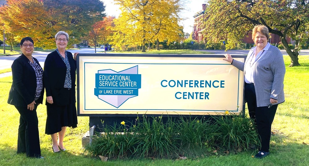 Three women standing outside in front of a sign that reads, "Conference Center".